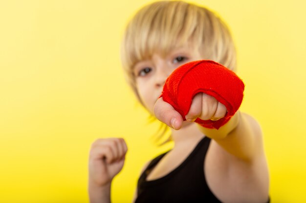 Una vista frontal chico rubio adorable boxeo en camiseta negra en la pared amarilla