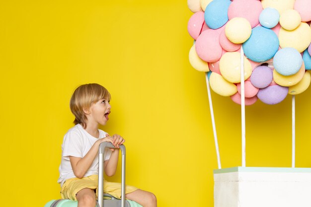 Vista frontal chico rubio con camiseta blanca y pantalones cortos amarillos junto con globos de colores en el amarillo