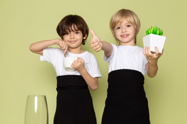 Una vista frontal chicos lindos sonriendo sosteniendo una pequeña planta verde y café en el piso de color piedra