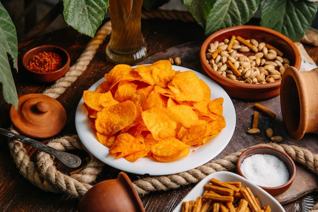 Una vista frontal de chips de naranja con maní y sal en la mesa de madera, chips de aperitivo, sal, especias