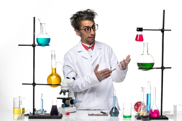 Vista frontal científico masculino en traje médico blanco de pie frente a la mesa con soluciones