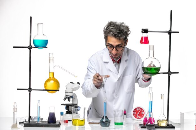 Vista frontal científico masculino en traje médico que trabaja con una solución azul en el fondo blanco claro virus de laboratorio salud coronavirus