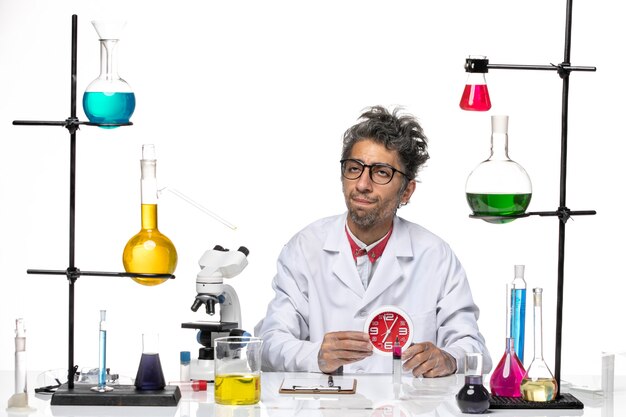 Vista frontal científico masculino en traje médico sosteniendo relojes rojos sobre fondo blanco claro química laboratorio covid virus salud