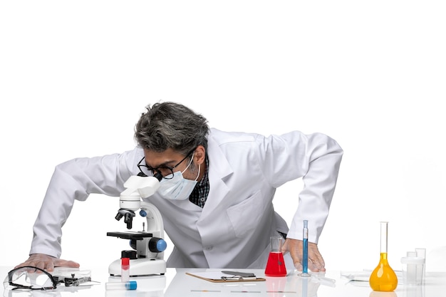 Vista frontal científico de mediana edad en traje blanco especial con microscopio