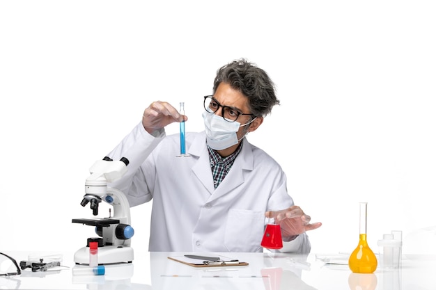 Vista frontal científico de mediana edad en traje especial sentado sosteniendo frascos con soluciones