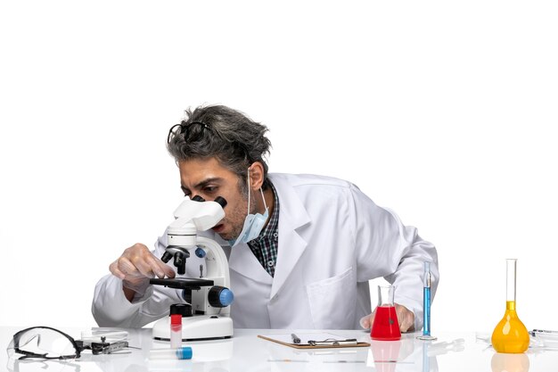 Vista frontal científico de mediana edad en traje médico blanco con microscopio