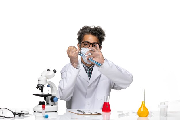 Vista frontal científico de mediana edad en traje médico blanco que llena la inyección con una solución azul