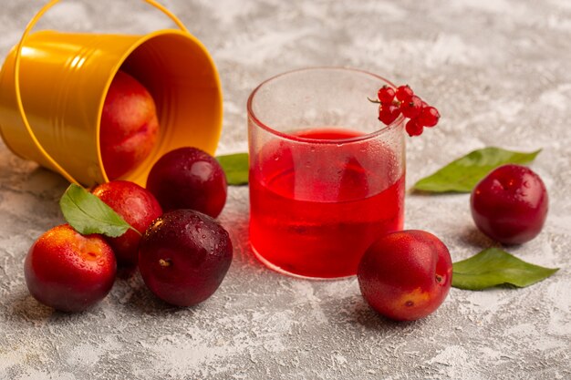 Vista frontal de ciruelas agrias frescas con escritorio de jugo de ciruela roja