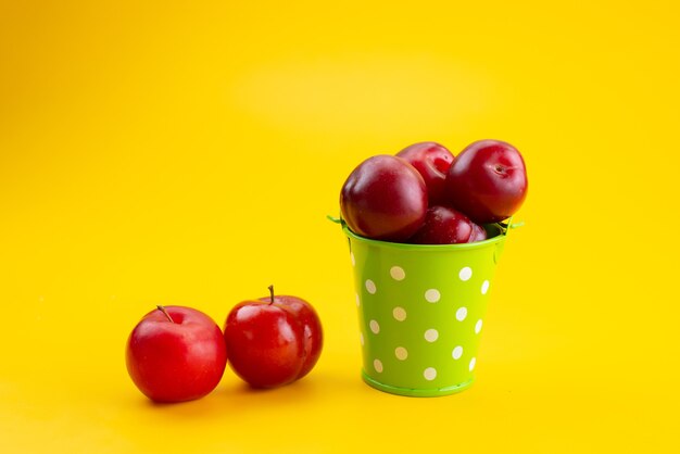 Una vista frontal de ciruelas rojas frescas dentro de la canasta verde en amarillo, color de fruta agria