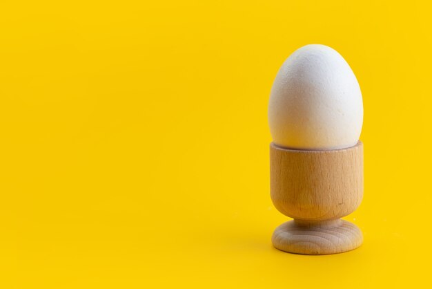 Una vista frontal de clara de huevo hervida, entera y dentro de un pequeño soporte en amarillo, color de comida