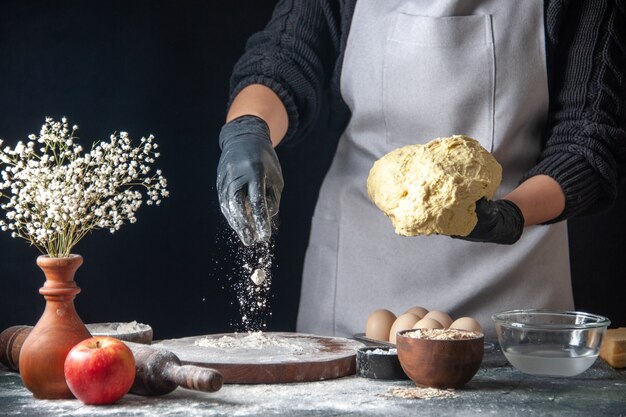 Vista frontal cocinera extendiendo la masa con harina en la oscuridad trabajo masa pastelería cocina hotcake cocina panadería huevo