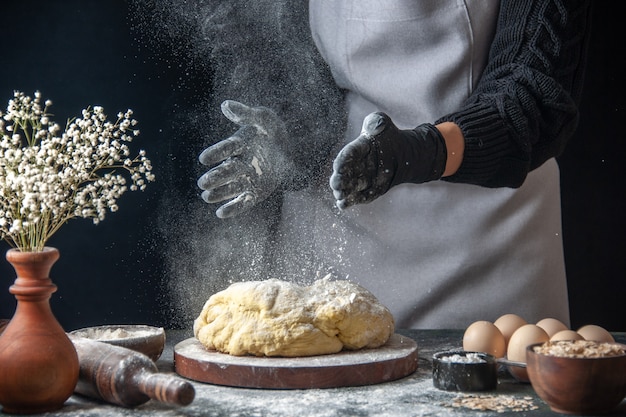 Vista frontal cocinera extendiendo la masa con harina en el oscuro trabajo masa cruda panadería horno de tarta pastelería hotcake