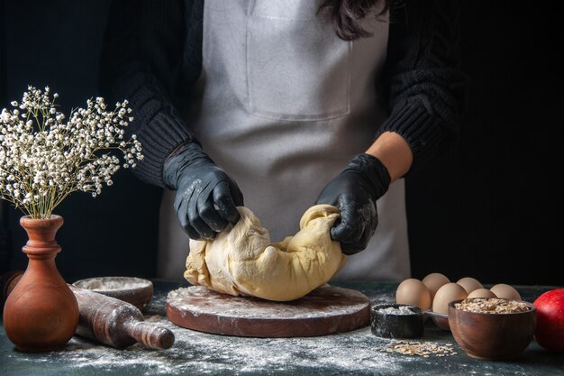 Vista frontal cocinera extendiendo la masa en el oscuro trabajo de pastelería hotcakes de masa cruda horno de tarta de panadería