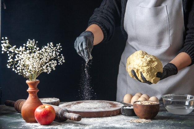 Vista frontal cocinera extendiendo la masa en el trabajo oscuro horno de tarta de masa cruda pastelería hotcake huevos de panadería