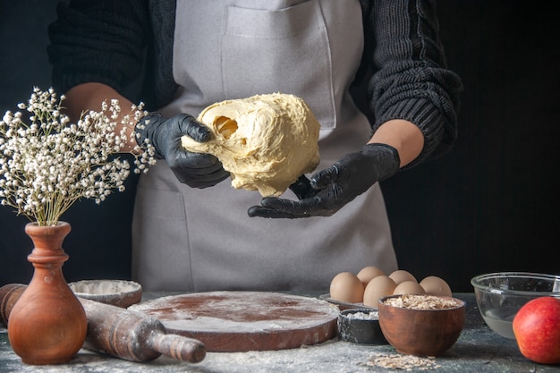 Vista frontal cocinera extendiendo la masa en el trabajo oscuro horno de tarta de masa cruda pastelería hotcake panadería huevo