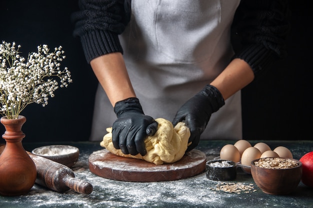 Foto gratuita vista frontal cocinera extendiendo la masa en el trabajo oscuro masa cruda hotcake panadería pastelería horno de tarta