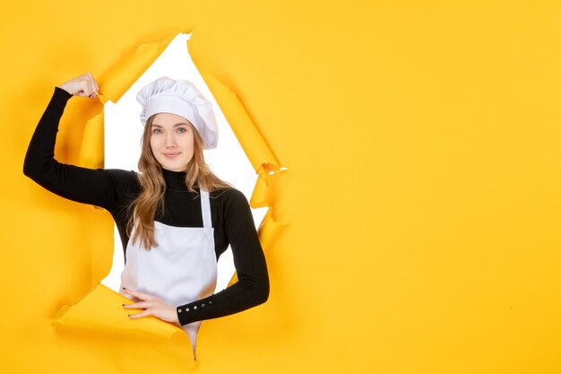 Vista frontal cocinera flexionando y sonriendo en amarillo emoción papel de color trabajo cocina sol comida foto