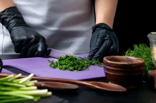 Vista frontal cocinera haciendo sabrosas ensaladas verdes de corte sobre un fondo oscuro cocina vacaciones trabajo comida comida trabajo cocina de color