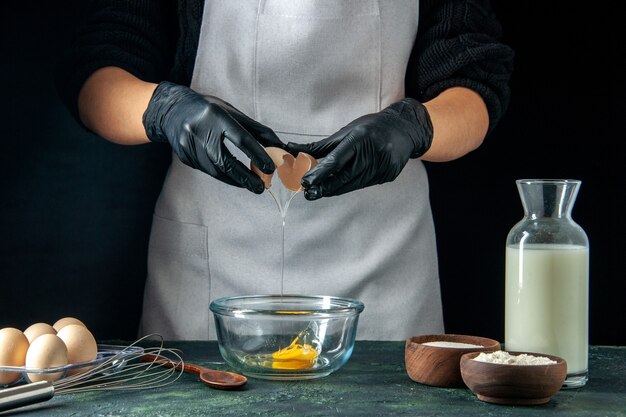 Vista frontal de la cocinera rompiendo los huevos para la masa en el trabajo de pastelería oscuro pastel pastel panadería trabajador cocina