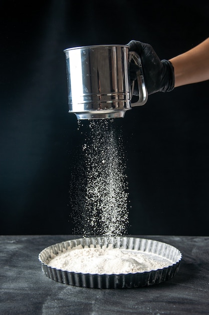 Foto gratuita vista frontal cocinera sembrando harina blanca en una sartén sobre pastel de huevo oscuro trabajo de trabajador de pastelería de pastel de cocina