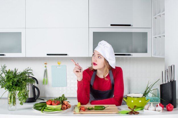 Vista frontal de la cocinera con sombrero de cocinero apuntando a la izquierda en la cocina