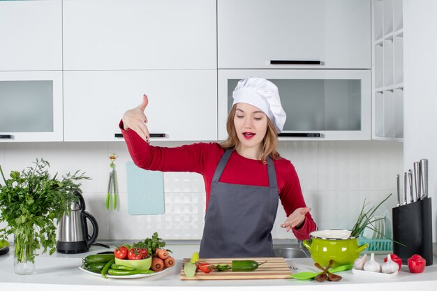 Vista frontal de la cocinera con sombrero de cocinero apuntando a la tabla de cortar