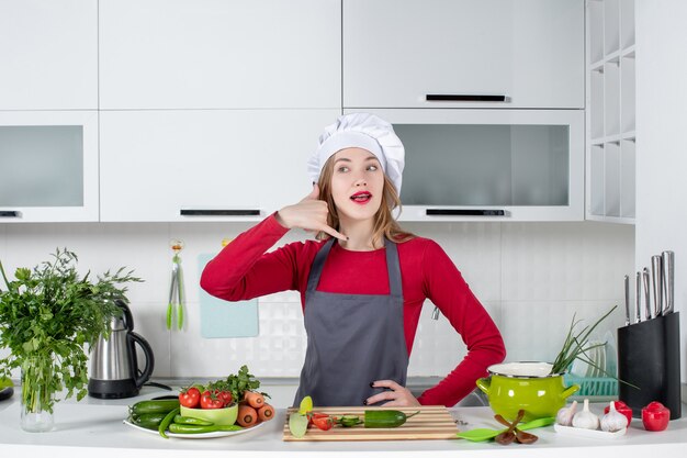 Vista frontal de la cocinera en sombrero de cocinero haciendo gesto de llamarme teléfono