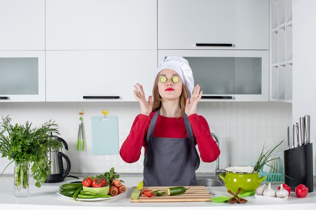 Vista frontal de la cocinera con sombrero de cocinero poniendo rodajas de pepino en los ojos en la cocina