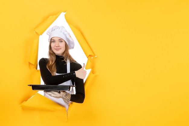 Vista frontal cocinera sosteniendo pan negro con galletas en amarillo emoción sol comida foto trabajo cocina cocina colores