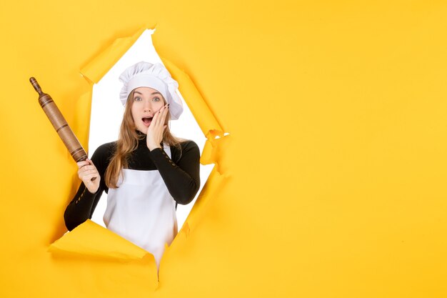 Vista frontal cocinera sosteniendo un rodillo en amarillo sol comida color cocina trabajo foto emoción