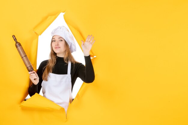 Vista frontal cocinera sosteniendo un rodillo sobre color amarillo comida cocina trabajo cocina foto emoción