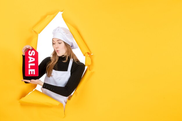 Vista frontal cocinera sosteniendo rojo venta escribiendo en el color amarillo trabajo cocina emoción comida foto cocina