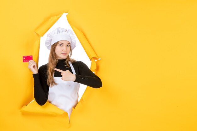 Vista frontal cocinera sosteniendo una tarjeta bancaria roja en color amarillo dinero foto de trabajo cocina cocina emoción comida