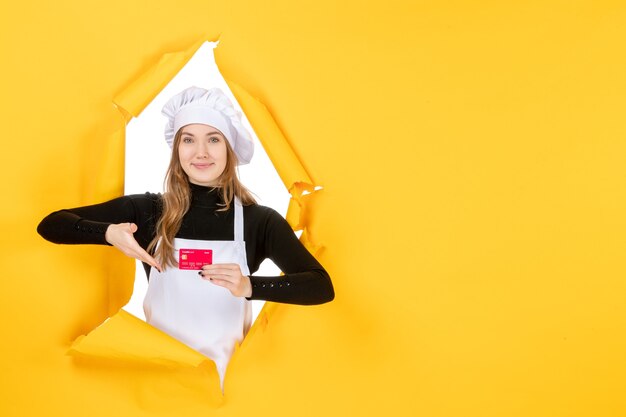 Vista frontal cocinera sosteniendo una tarjeta bancaria roja en color amarillo dinero foto de trabajo comida cocina cocina emoción