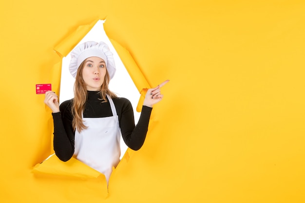 Vista frontal cocinera sosteniendo una tarjeta bancaria roja en color amarillo dinero trabajo comida cocina cocina emoción