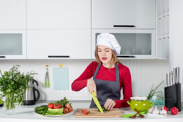 Vista frontal cocinera trabajadora en delantal cortando pepino