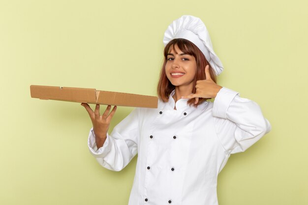 Vista frontal cocinera en traje de cocinero blanco con caja de comida en el escritorio verde
