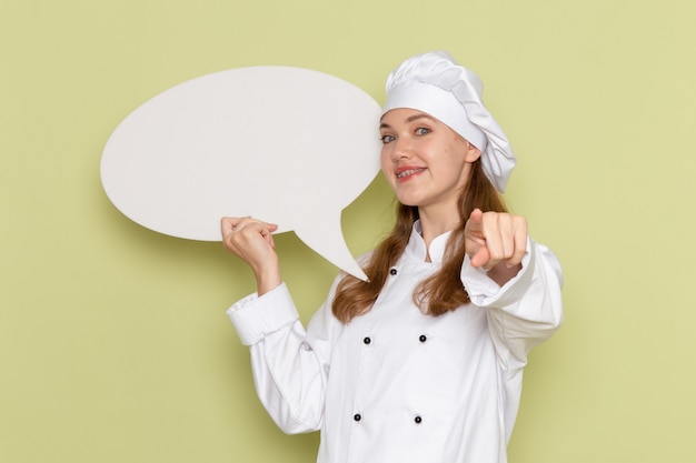 Vista frontal de la cocinera en traje de cocinero blanco con gran cartel blanco en la pared verde
