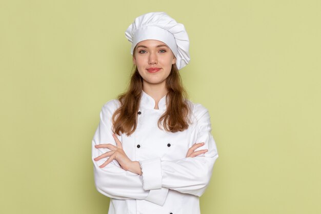 Vista frontal de la cocinera en traje de cocinero blanco sonriendo posando en la pared verde