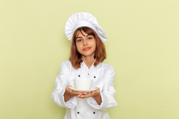 Vista frontal cocinera en traje de cocinero blanco sosteniendo una taza de té en la superficie verde