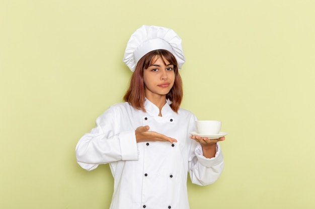 Vista frontal cocinera en traje de cocinero blanco sosteniendo una taza de té en la superficie verde