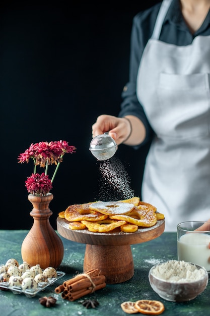 Vista frontal cocinera vertiendo azúcar en polvo en anillos de piña secos en fruta oscura trabajo de cocina pastelería pastel pastel panadería