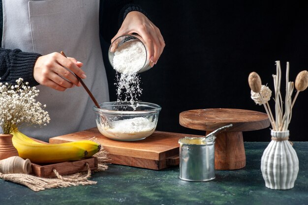 Vista frontal cocinera vertiendo coco en un plato con leche condensada sobre fondo oscuro