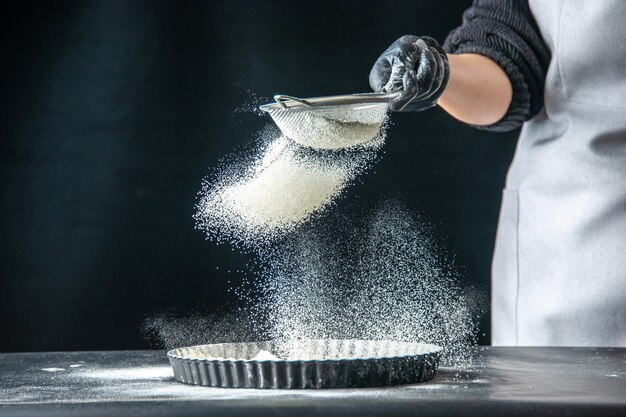 Vista frontal cocinera vertiendo harina blanca en la sartén en un huevo oscuro trabajo panadería hotcake pastelería cocina masa de cocina
