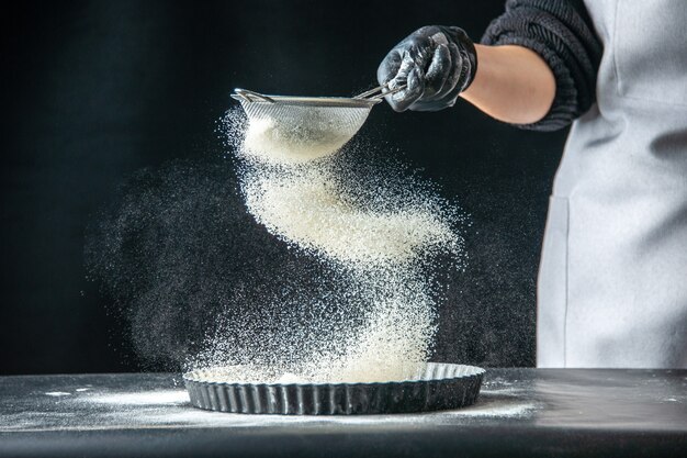 Vista frontal cocinera vertiendo harina blanca en la sartén sobre huevo oscuro trabajo panadería pastelería cocina masa de cocina