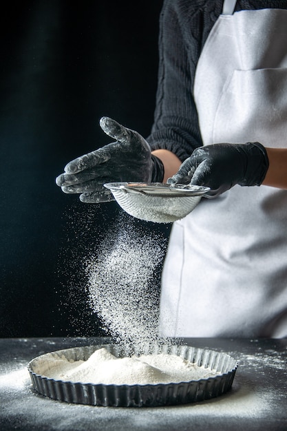 Vista frontal cocinera vertiendo harina blanca en la sartén sobre pastel de huevo oscuro panadería pastelería cocina cocina masa hotcake