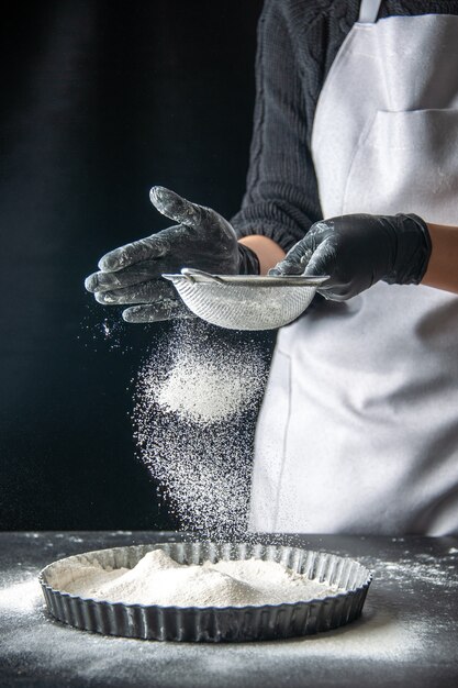 Vista frontal cocinera vertiendo harina blanca en la sartén sobre pastel de huevo oscuro panadería pastelería cocina masa tarta hotcake