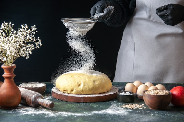 Vista frontal cocinera vertiendo harina blanca sobre masa cruda en oscuro trabajo de pastelería masa cruda hotcake panadería horno de tarta