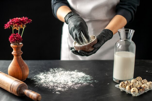 Vista frontal cocinera vertiendo harina blanca sobre la mesa para la masa en el trabajo de frutas oscuras pastel de pastelería pastel de panadería cocinar
