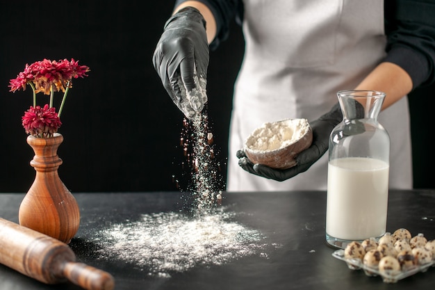 Vista frontal cocinera vertiendo harina blanca sobre la mesa para la masa en el trabajo de frutas oscuras pastelería pastelería panadería cocinar
